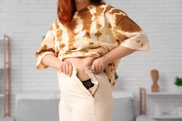 Image of woman trying to do her trousers up after pregnancy weight gain Sutton