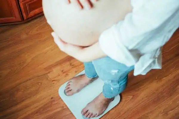 Image of woman weighing herself and experiencing weight gain through pregnancy Sutton